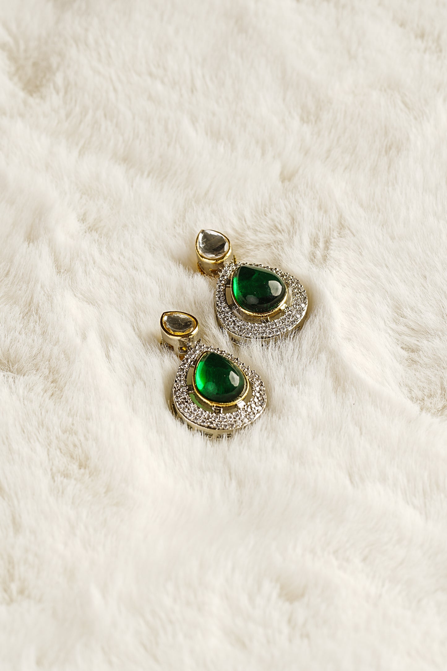 Pair of earrings with green gemstones on a white fur background
