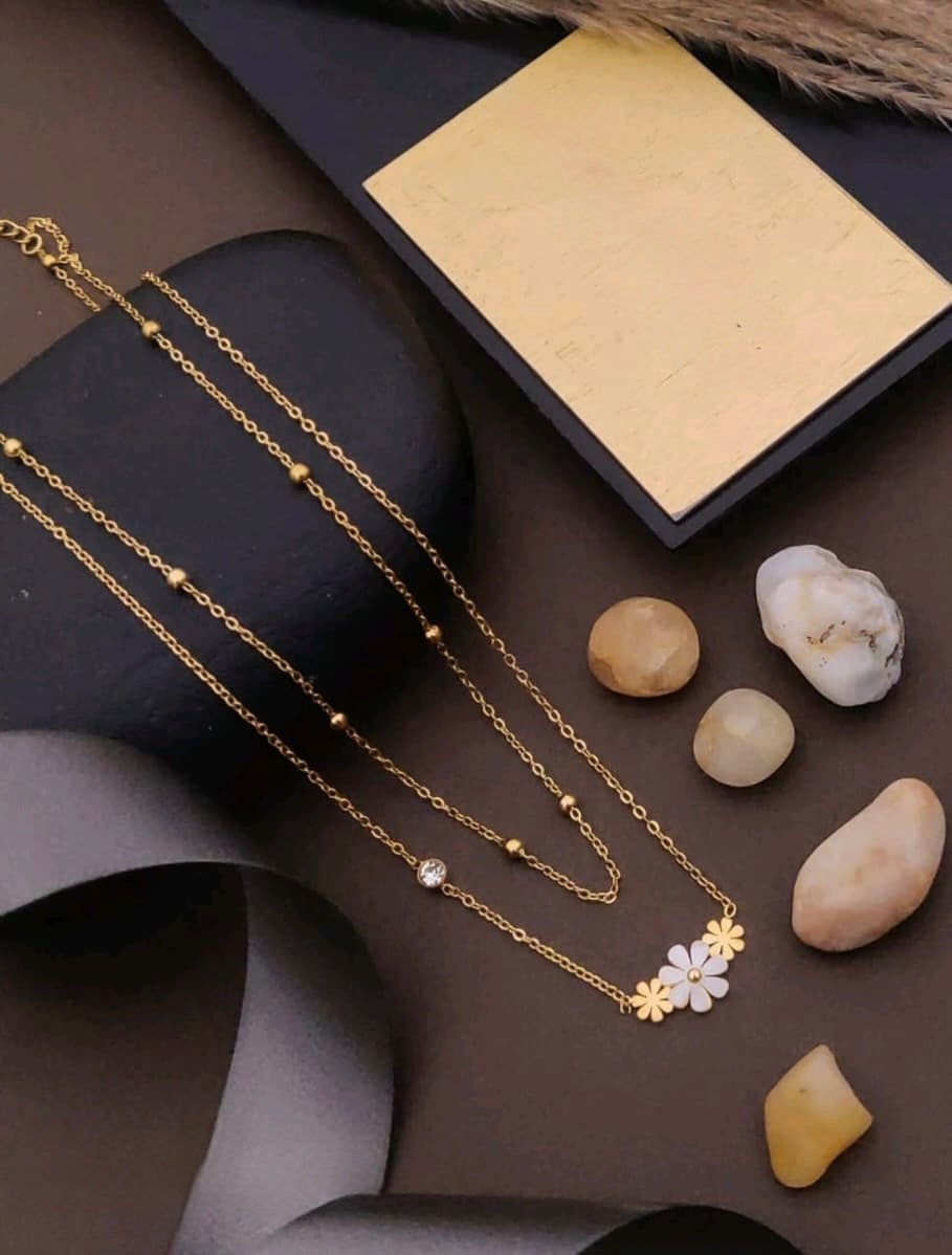 Gold necklace with a floral pendant on a dark surface with stones