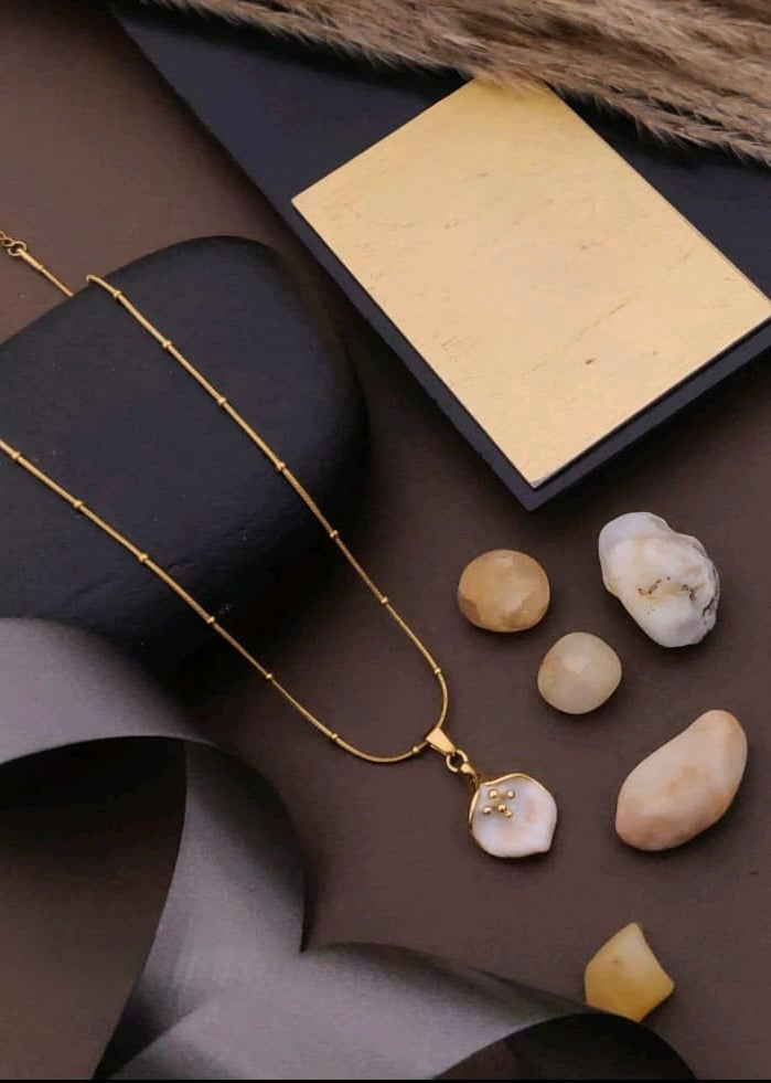 Gold necklace with a pendant on a dark surface with stones