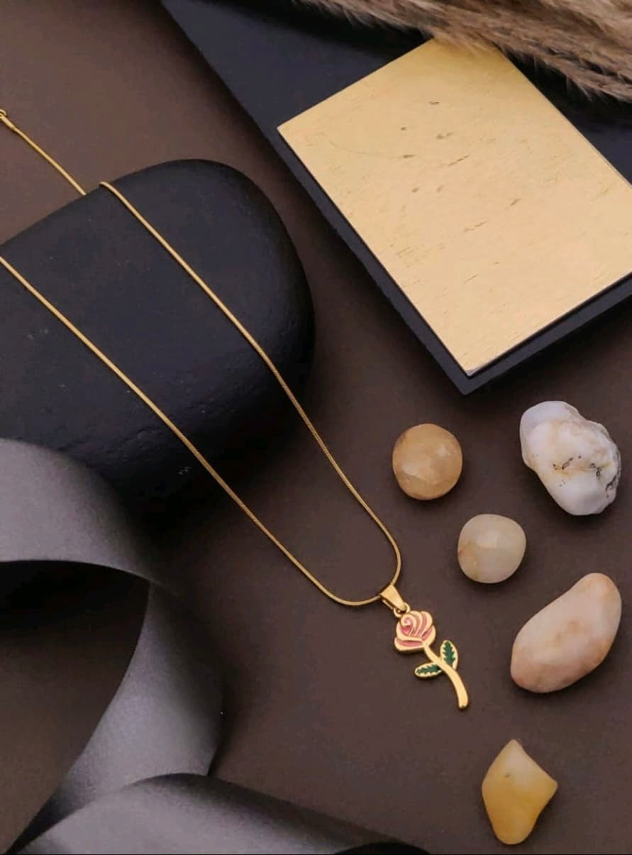 Gold necklace with a rose pendant on a dark surface with stones