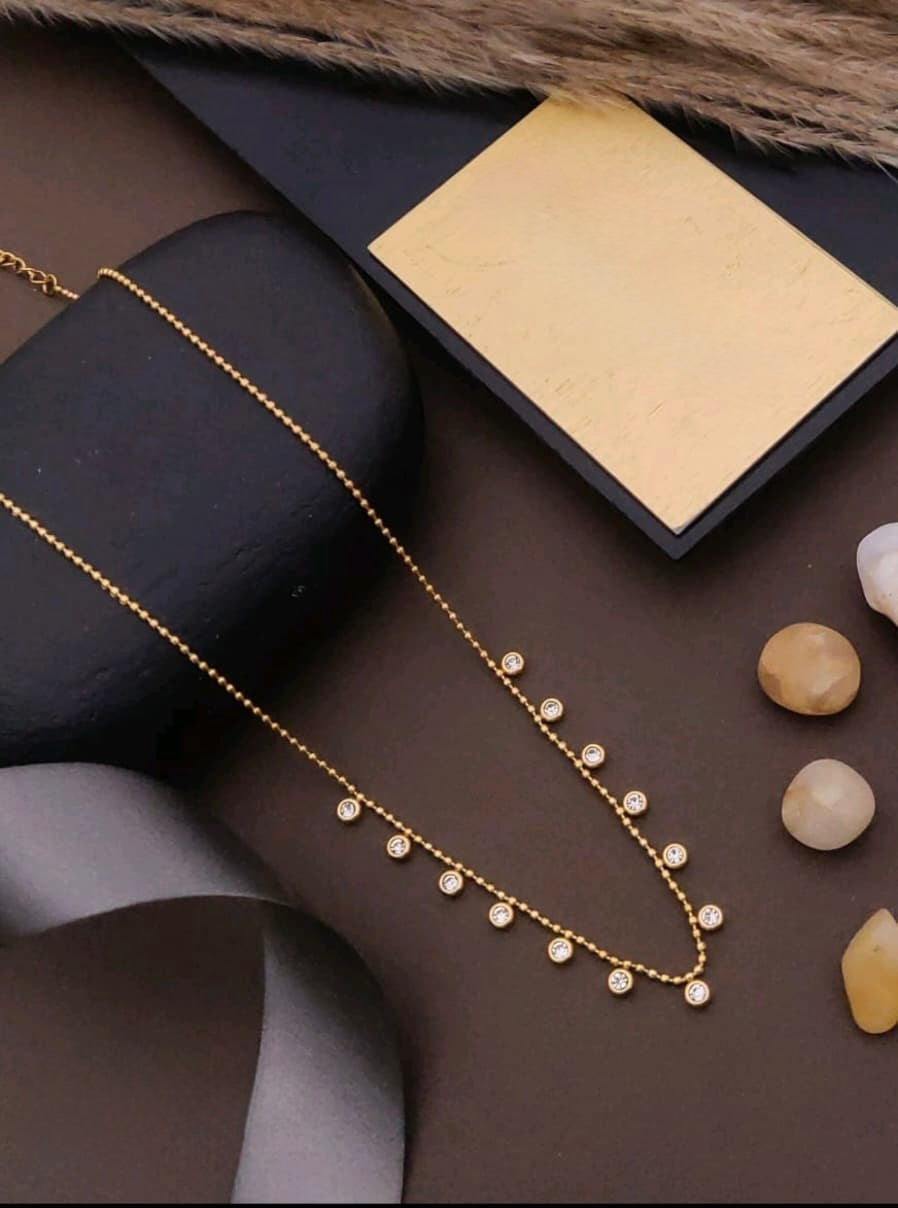 Gold necklace with small beads on a dark surface with stones