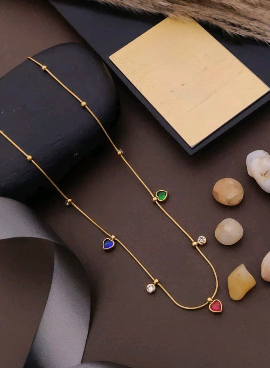 Gold necklace with colorful heart-shaped pendants on a dark surface with stones.