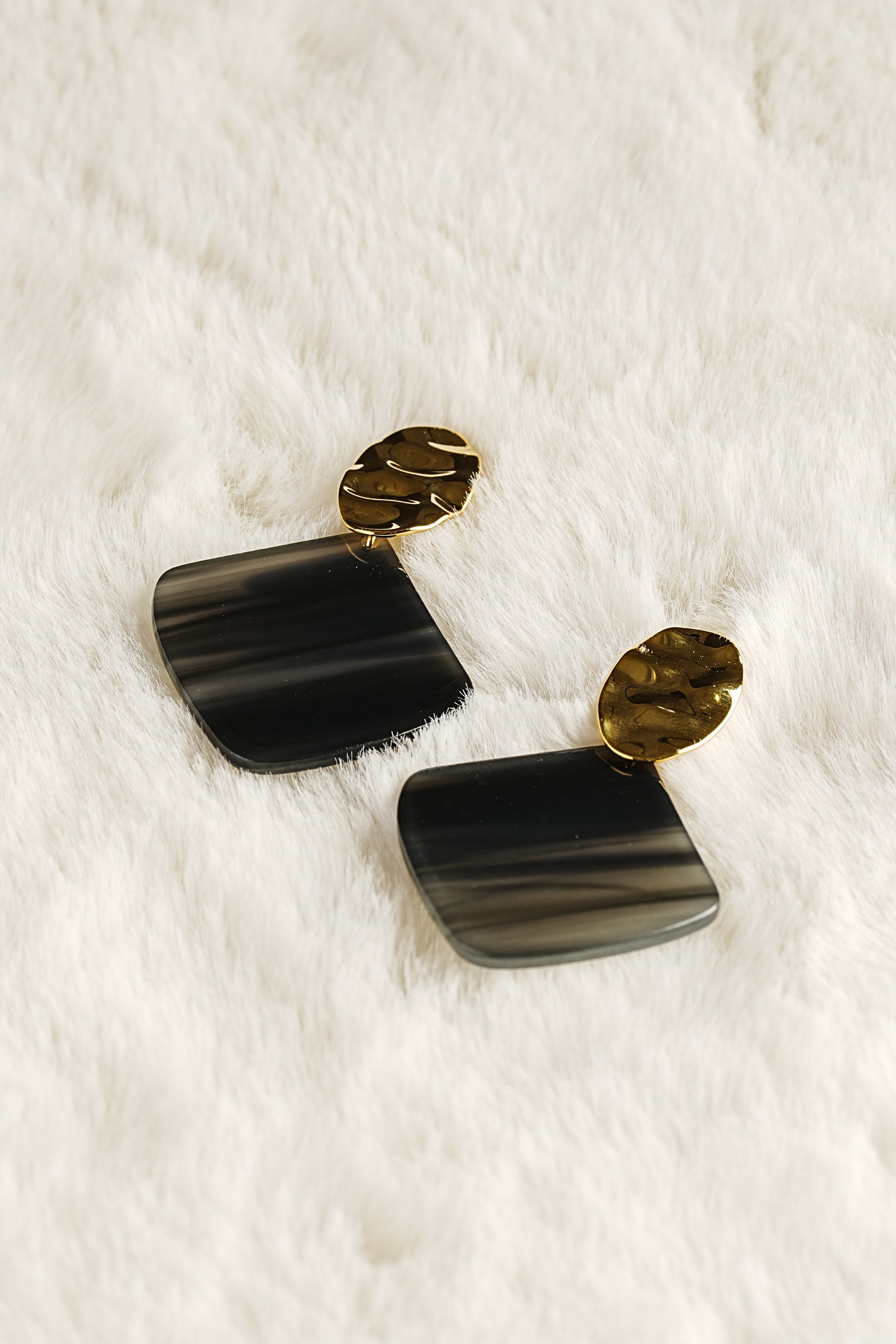 Black and gold earrings on a white fur background