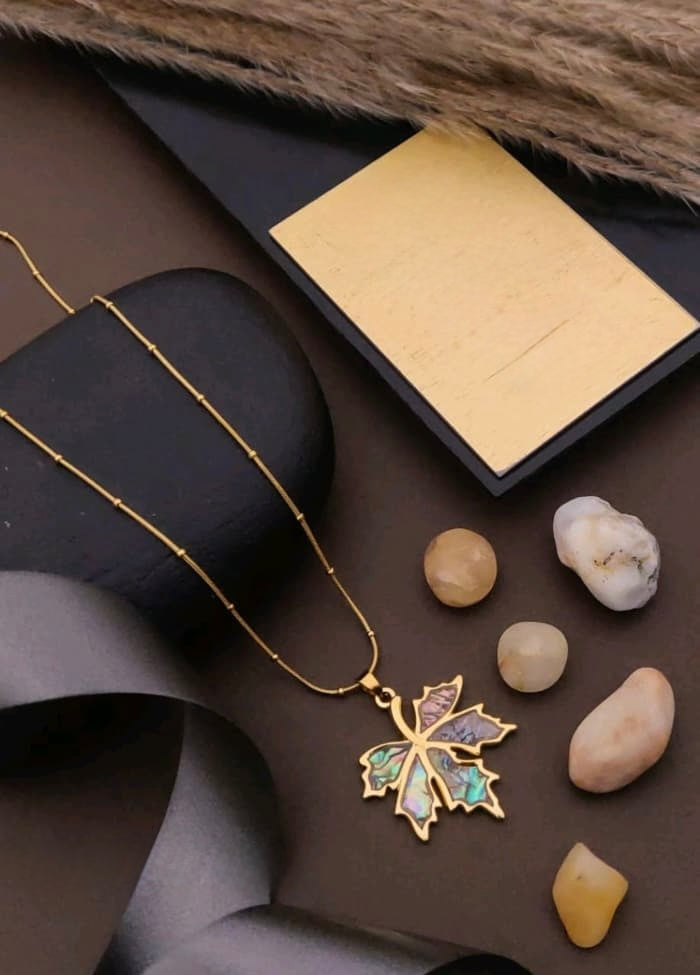 Gold necklace with a leaf pendant on a dark surface with stones