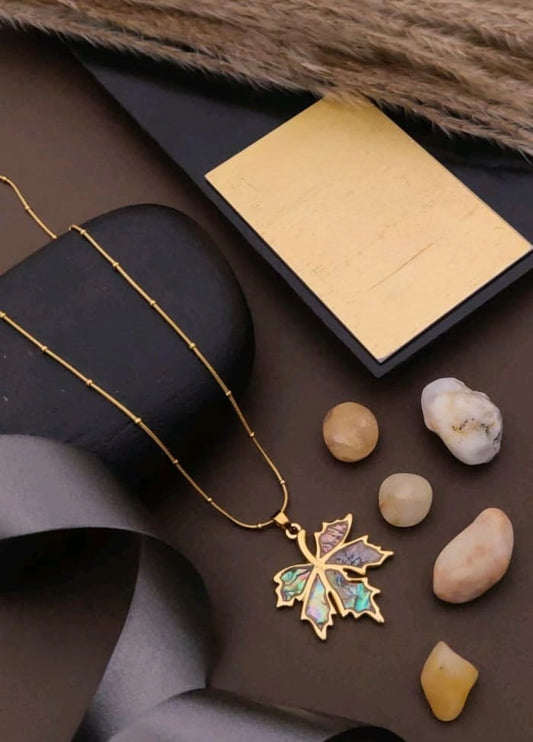 Gold necklace with a leaf pendant on a dark surface with stones