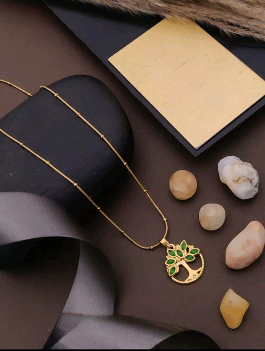 Gold necklace with a tree pendant on a dark surface with stones
