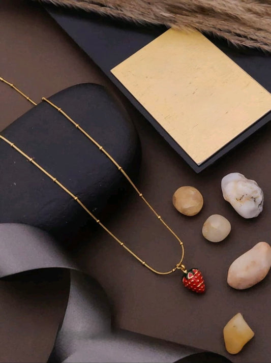 Gold necklace with a strawberry pendant on a dark surface with stones