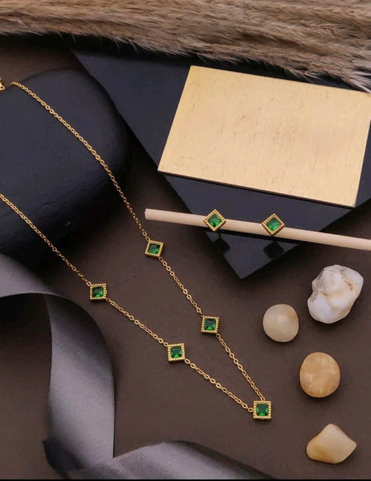 Gold necklace with green gemstones on a dark surface with a gold box and stones.