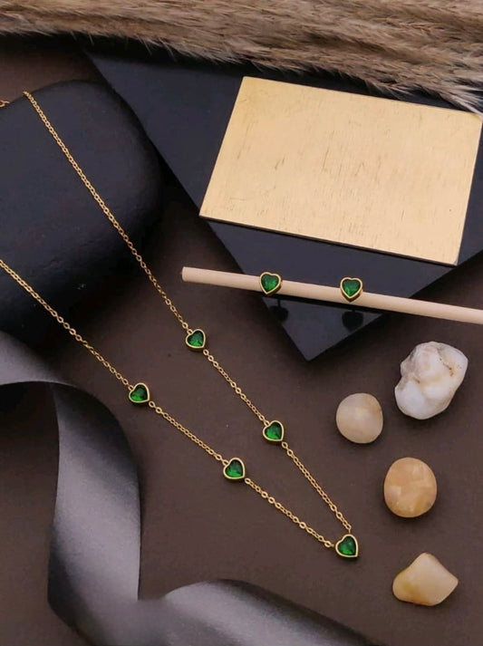 Gold necklace with green heart-shaped stones on a dark surface with a gold box and stones.