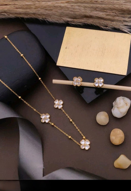 Gold necklace with floral pendants on a dark surface with stones and a box.