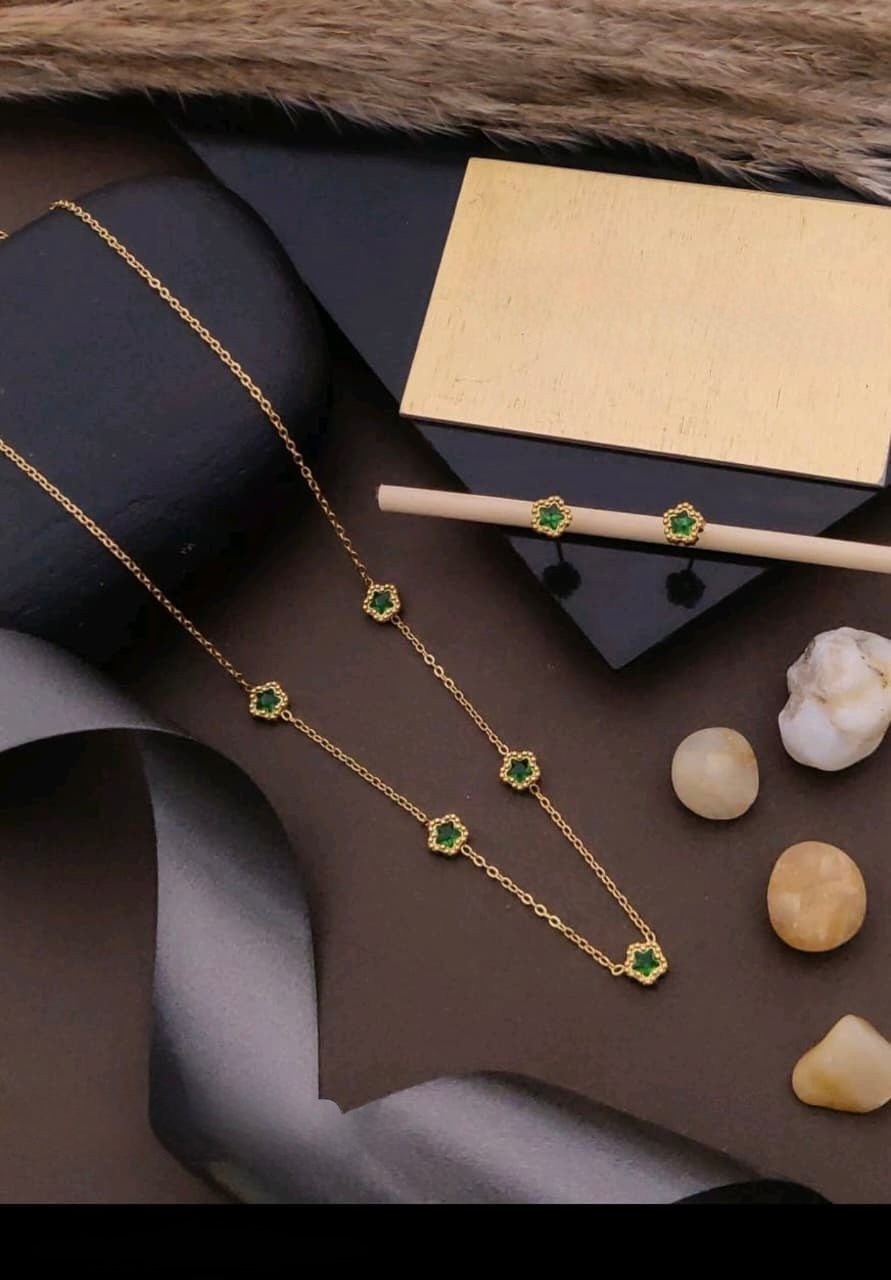Gold necklace with green gemstones on a dark surface with a box and decorative items.