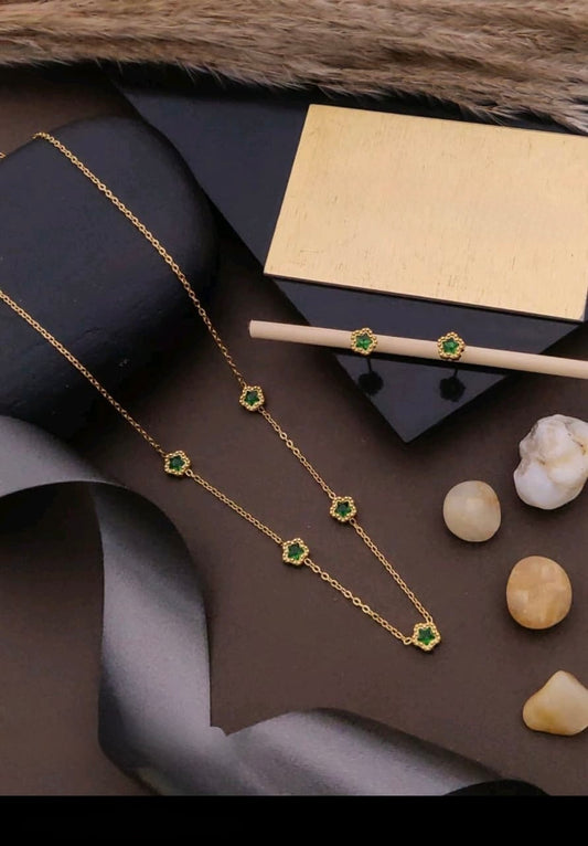 Gold necklace with green gemstones on a dark surface with a box and decorative items.